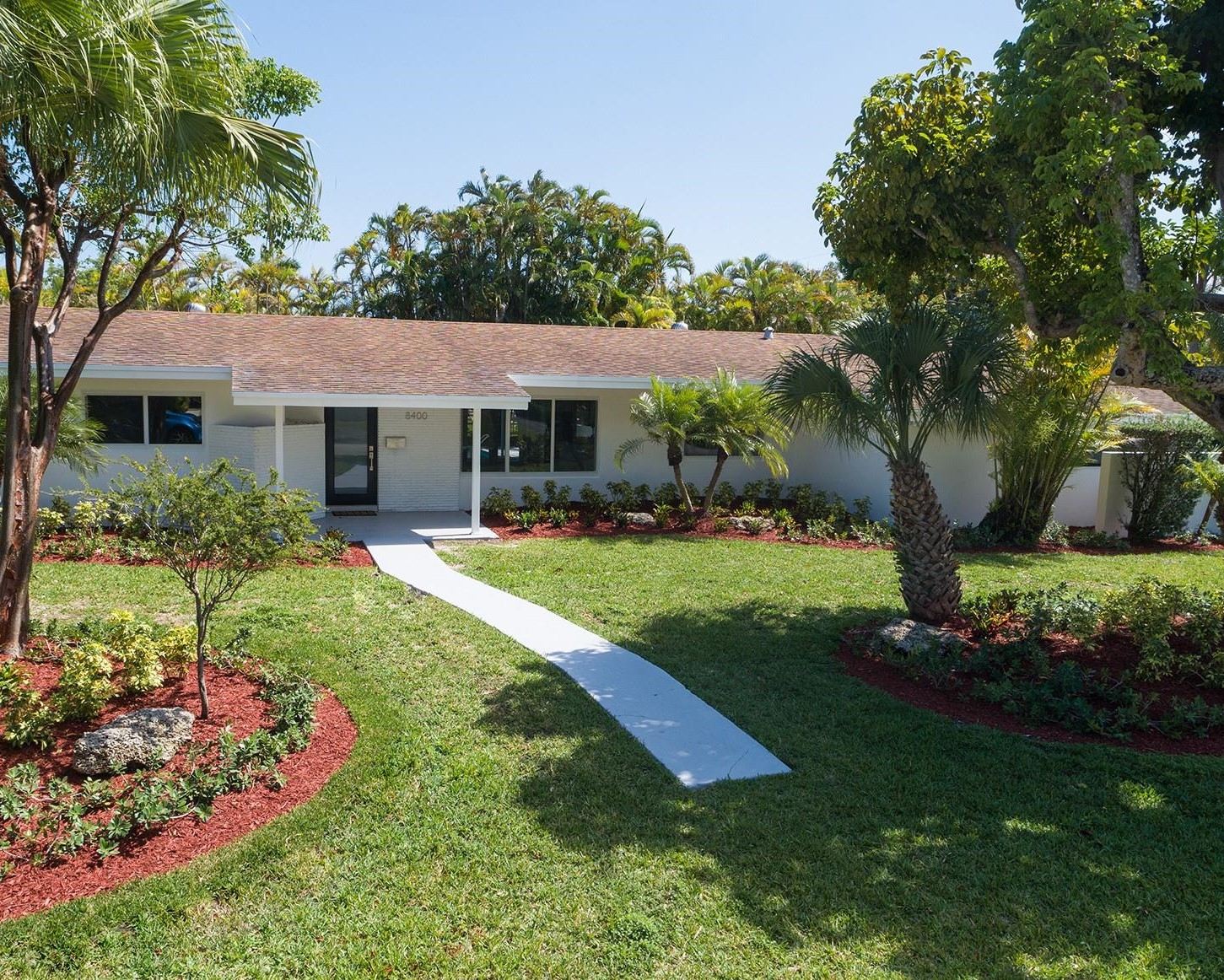 Single-story South Florida home exterior with painted stucco walls, wide window openings, and a shingle roof after renovation